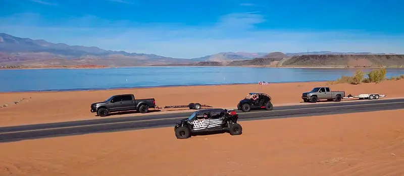 ORVs pass parked trucks on road next to reservoir in Sand Hollow State Park in Utah