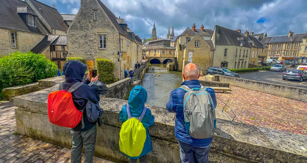 Tourists in rain gear view Bayeux canal and houses on our free virtual walks for treadmills